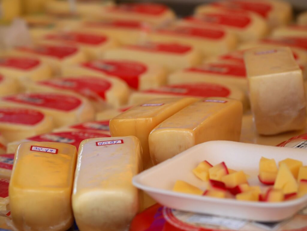 Variety of cheese blocks and samples on display at a market stall.